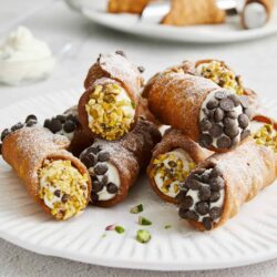 Fresh cannoli with ricotta filling, chocolate chips, and pistachios on a white plate.