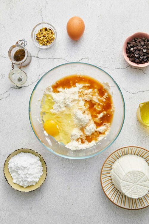 Cream cheese, eggs, and sugar ingredients for baking on a white textured surface.