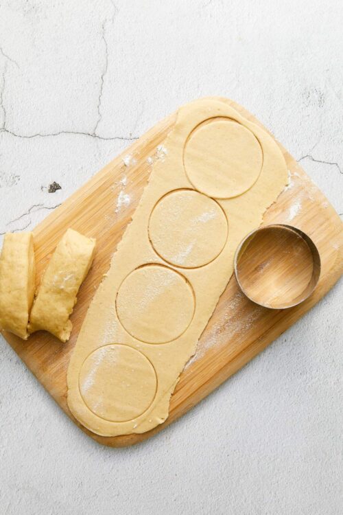 Buttery pie dough rolled out with cookie cutter on wooden board.
