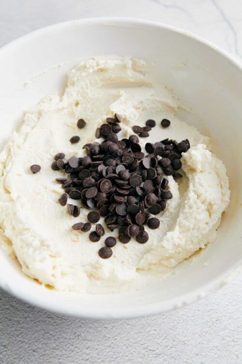 Cream cheese with chocolate chips in a white bowl, ready to make desserts or baked goods.