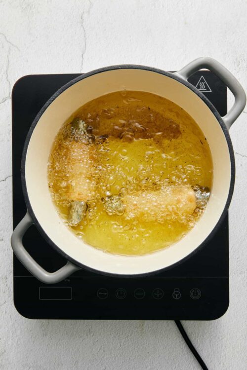 Golden fried chicken cooking in a skillet on an electric stovetop.