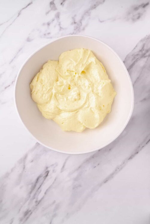 Creamy homemade butter in a white bowl on marble surface.