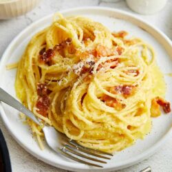 Garlic butter spaghetti with bacon and grated cheese on white plate.