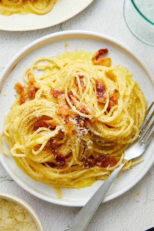 Creamy bacon carbonara pasta with grated cheese and black pepper in a white dish.