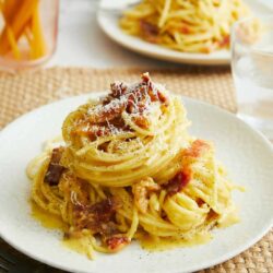 Creamy bacon carbonara pasta with grated cheese on white plate.