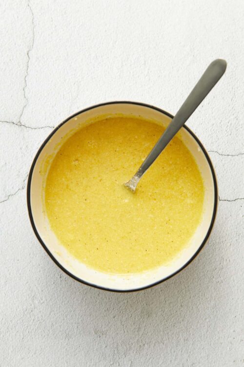 Creamy yellow sauce in a bowl with a spoon, on a white textured surface, perfect for baking recipes.