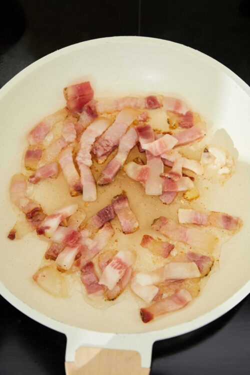 Sizzling bacon in a white skillet for breakfast or cooking.