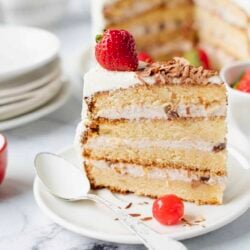 Delicious layered vanilla and chocolate birthday cake with strawberries and whipped cream on a white plate.