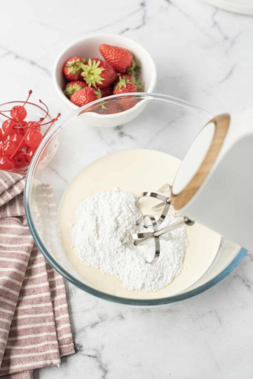 Fresh strawberries and cherries in bowls with beaters mixing cream and sugar for strawberry shortcake or dessert.