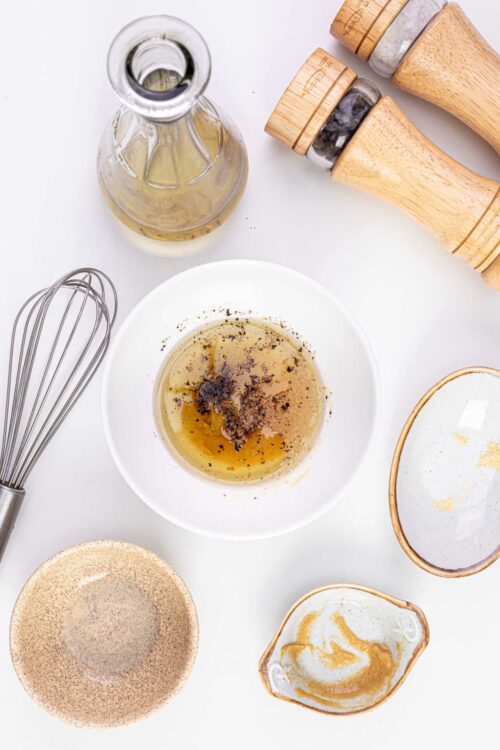 Vinaigrette ingredients with oil, vinegar, salt, pepper, and utensils on white background.