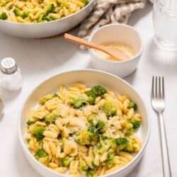 Creamy broccoli cheese pasta in a white bowl, served with grated cheese and fresh broccoli florets.