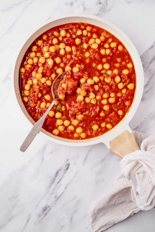 Creamy chickpea and tomato stew in a white skillet on marble surface.