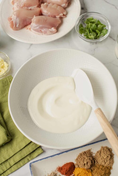 Creamy white sauce in a white bowl with a wooden spoon on a marble countertop.