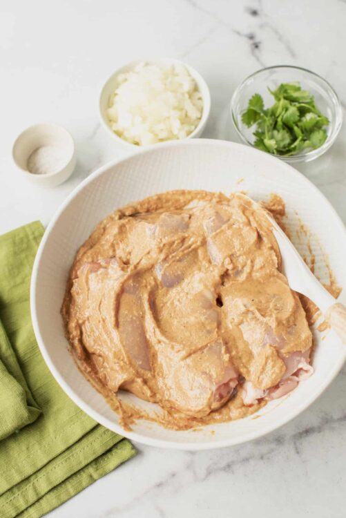 Raw chicken marinating in a bowl with a spicy sauce for baking.
