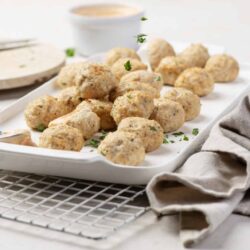 Creamy chicken meatballs on white platter garnished with parsley, served with dipping sauce, baked for comfort food.