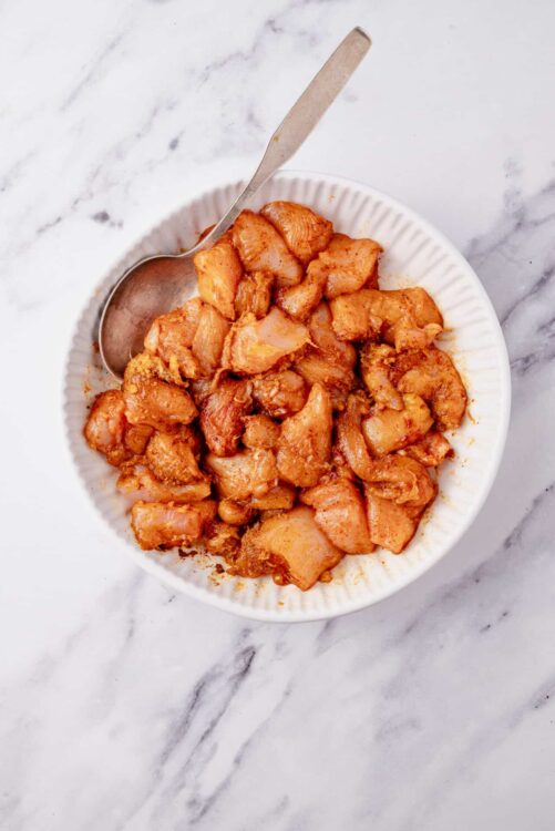 Marinated diced chicken in a white bowl on marble surface.
