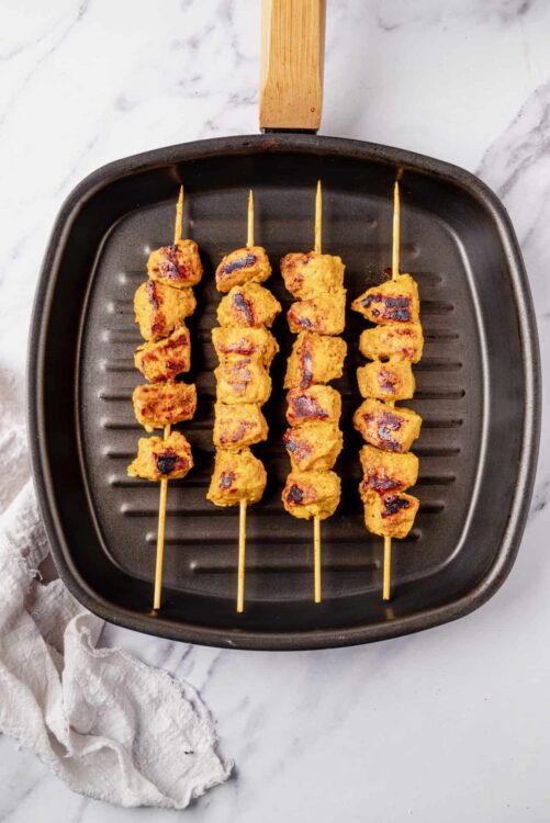 Skewered grilled chicken with a golden marinade on a cast iron grill pan.