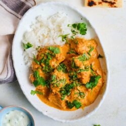Creamy chicken curry served with white rice and cilantro on a white dish.