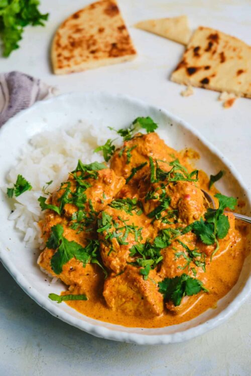 Creamy chicken curry served with white rice, garnished with fresh cilantro, on a white dish.