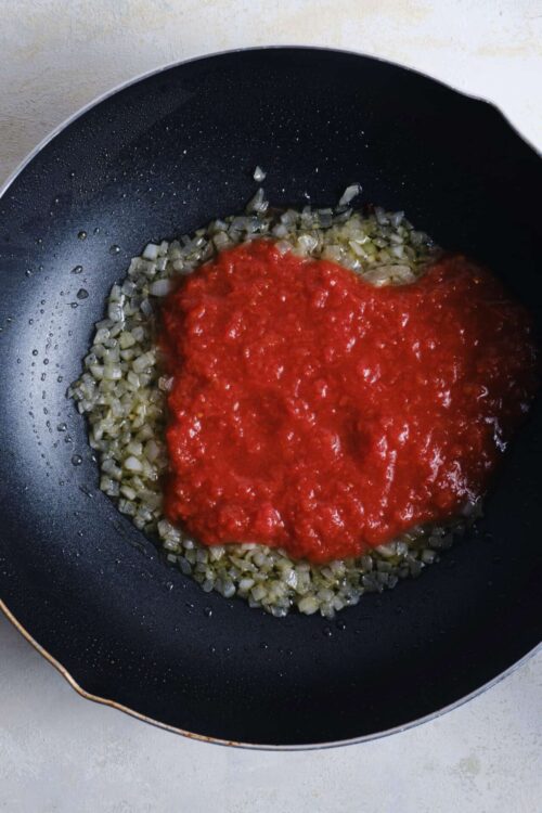 Sautéed onions with tomato sauce cooking in a skillet for homemade recipes.