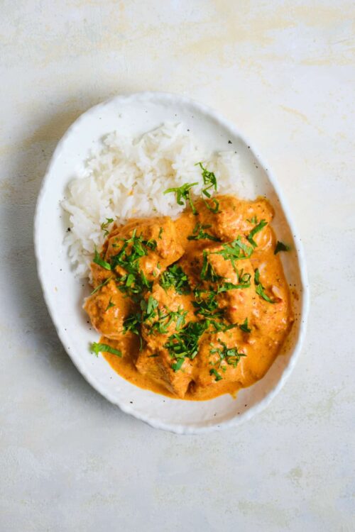 Creamy chicken curry with white rice garnished with fresh cilantro on a white plate.