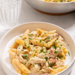 Creamy chicken Alfredo pasta with penne and herbs, served in a white bowl.