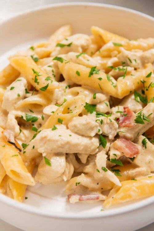 Creamy chicken and pasta Alfredo with parsley garnish on a white plate.