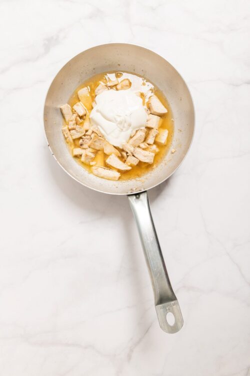 Creamy chicken and mushroom sauce cooking in a stainless steel skillet, featuring tender chicken pieces, cream, and mushroom broth.