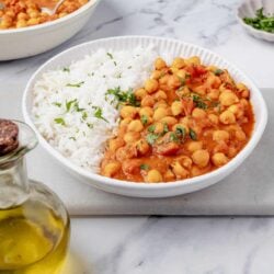 Creamy chickpea curry served with fluffy white rice on a white plate. Perfect vegetarian meal with fresh herbs and flavorful tomato sauce.
