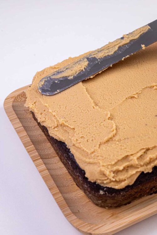 Creamy peanut butter frosting spread on chocolate brownie cake, with a spatula for frosting application.