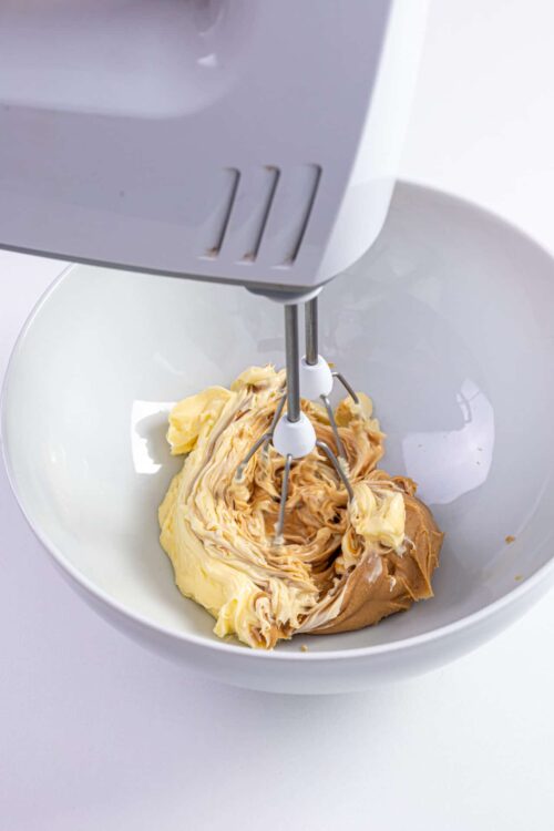 Creamy peanut butter and butter in a mixing bowl with a hand mixer for baking or dessert recipes.