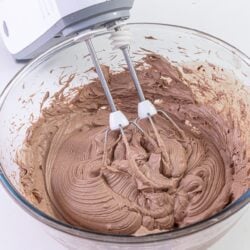Creamy chocolate cake batter in a glass mixing bowl with an electric hand mixer.