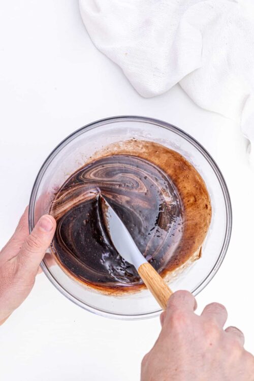 Creamy chocolate ganache being stirred in glass bowl for baking recipes.