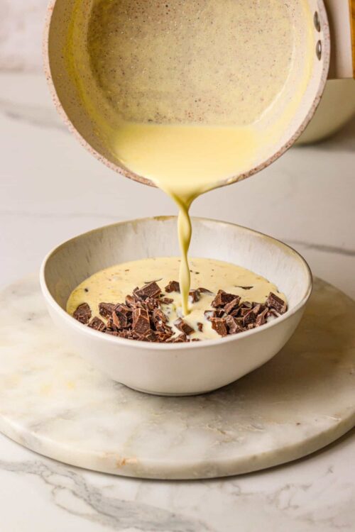Rich vanilla custard being poured into a bowl with chocolate chunks for a dessert recipe.