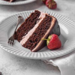 Rich chocolate cake with pink frosting and fresh strawberries on a white plate.