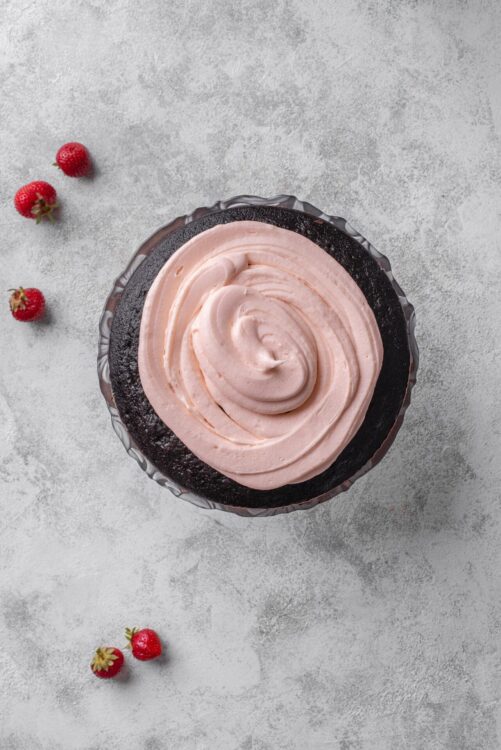 Rich chocolate cake with pink strawberry frosting, topped with swirled frosting, on a textured gray background.