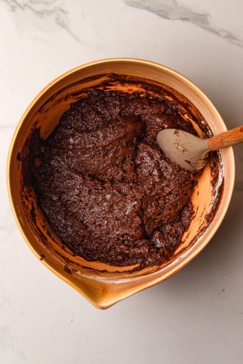Rich chocolate brownie batter in a mixing bowl with spatula, BakeBree recipe.