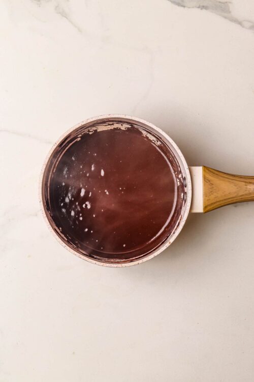 Silicone saucepan with wooden handle heating water on white countertop.