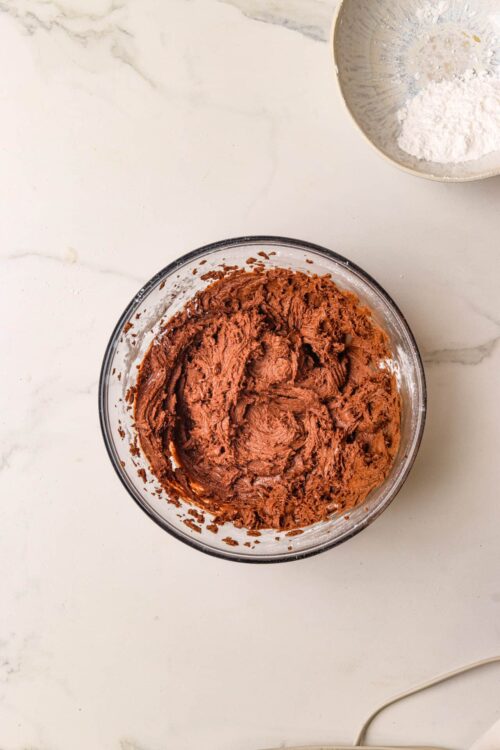 Rich chocolate cookie dough in a glass mixing bowl for baking desserts.
