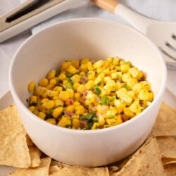 Corn salsa in a white bowl with tortilla chips on a platter.