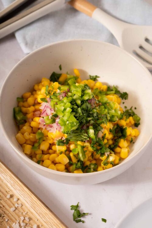 Fresh corn salad with chopped green onions and cilantro in a white bowl.
