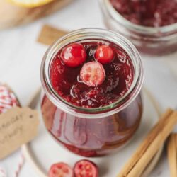 Sweet cranberry jelly in glass jar with cranberries and citrus.
