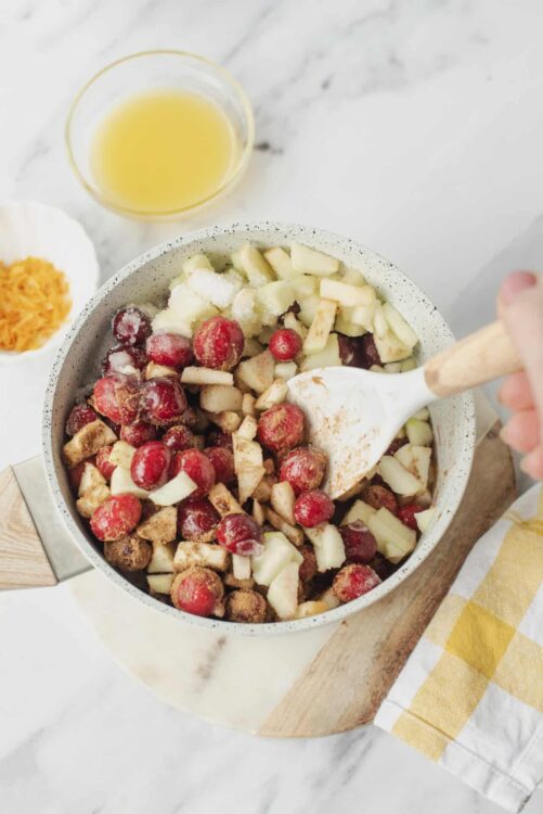 Fresh fruit being prepared for baking, including apples and cranberries, in a kitchen setting.
