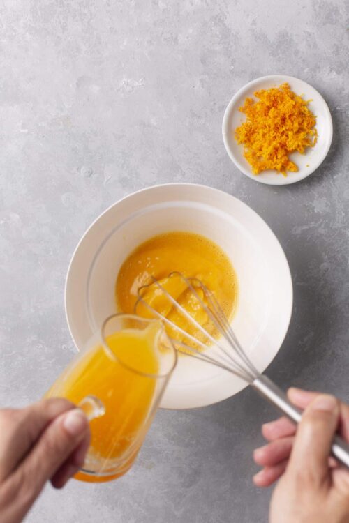 Fluffy scrambled eggs with orange juice and shredded cheddar cheese on white plates, breakfast, morning meal, baking process.