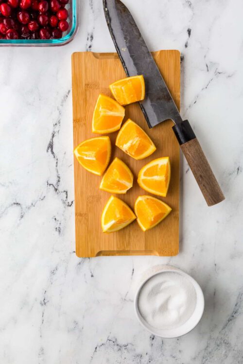 Juice from fresh orange wedges on a wooden cutting board with a chef's knife.