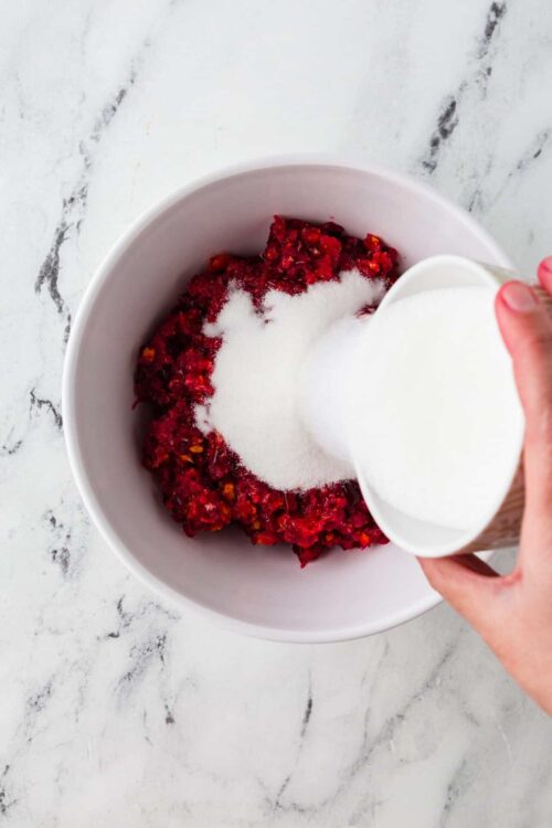 Fresh raspberry mixture with sugar being poured into a white bowl for baking.