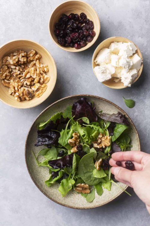 Fresh mixed greens salad topped with walnuts and dried cranberries, in preparation for a healthy meal or side dish.