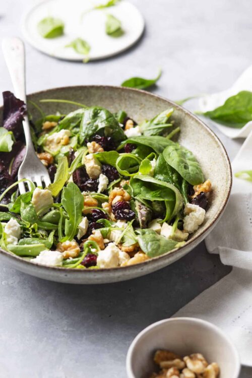 Fresh mixed greens salad with feta cheese, dried cranberries, and walnuts on a rustic plate.