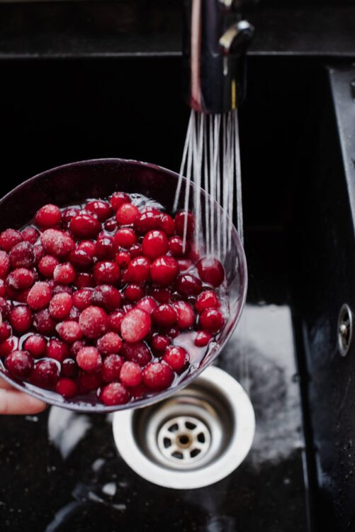 Fresh red berries being rinsed under a kitchen faucet for baking or cooking.