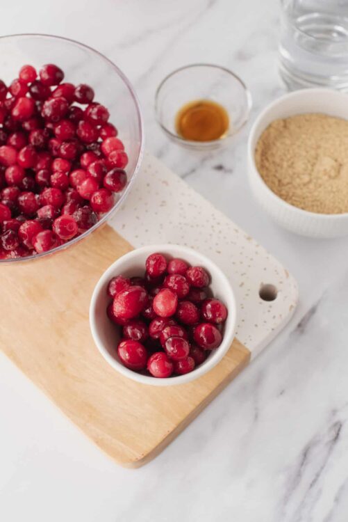 Fresh cranberries on a cutting board with sugar, honey, and other baking ingredients for cranberry recipes.